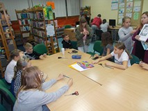 Dzieci siedzą przy stole i rozmawiają o pracy plastycznej do wykonania