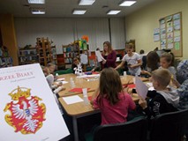 Dzieci siedzą przy stole a bibliotekarka wspiera pracę dzieci