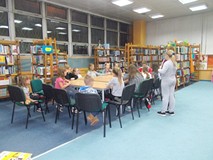 Dzieci siedzą przy stole i rozmawiają o symbolach narodowych z bibliotekarką