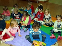 Dzieci siedzą na chuście integracyjnej  i oglądają wybrane przez siebie książeczki