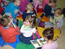 Dzieci siedzą na chuście integracyjnej  i oglądają wybrane przez siebie książeczki