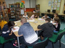 Dzieci siedzą przy stole i wykonują prace plastyczną