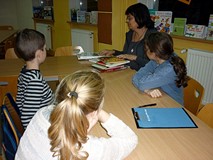 Dzieci siedzą przy stole, bibliotekarz prezentuje wybraną literaturę przedmiotu
