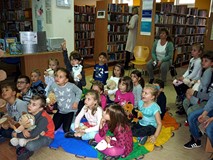 Dzieci siedzą na chuście i słuchają historii bibliotecznego pluszowego misia - ZNAJDKA