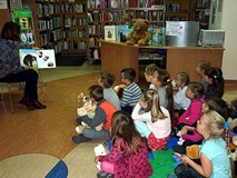 Dzieci siedzą na chuście integracyjnej, bibliotekarka czyta książeczkę D. Mellinga KTO PRZYTULI MISI
