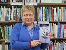 Autorka bloga z książką na tle regałów z książkami