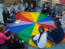 Dzieci siedzą na dywanie i słuchają andrzejkowego opowiadania czytanego przez bibliotekarza