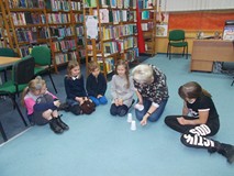 Dzieci siedzą w kole na dywanie podczas wpolnej zabawy z bibliotekarką