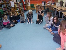 Dzieci siedzą w kole na dywanie podczas wpolnej zabawy z bibliotekarką