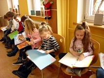 Dzieci siedzą na krzesełkach i przeglądają książki z wystawki BAJKOWE ŚWIĘTA