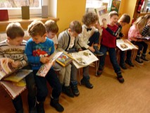 Dzieci siedzą na krzesełkach i przeglądają książki z wystawki BAJKOWE ŚWIĘTA