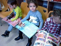 Przedszkolaki siedzą na krzesełkach i przeglądają świąteczne książeczki