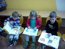 Przedszkolaki siedzą na krzesełkach i przeglądają świąteczne książeczki