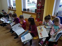 Przedszkolaki siedzą na krzesełkach i przeglądają świąteczne książeczki