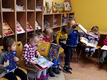 Przedszkolaki siedzą na krzesełkach i przeglądają świąteczne książeczki