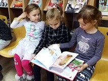 Dzieci siedzą na krzesełkach i przeglądają książeczki o tematyce świątecznej