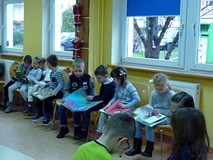 Dzieci siedzą na krzesełkach i przeglądają książeczki o tematyce świątecznej