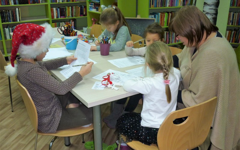 Uczestnicy zajęć wraz z bibliotekarką siedzą przy stoliku