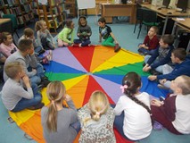 Dzieci siedzą w kole na chuście animacyjnej słuchając dzewczynki czytającej list od Mikołaja