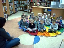 Dzieci siedzą na chuście animacyjnej i w wielkim skupieniu słuchają Pani Wioli, opowiadającej o św. 