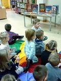 Dzieci siedzą na chuście animacyjnej i słuchają czytanej przez bibliotekarkę książeczki ŚWIĘTA PANA 
