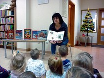 Dzieci siedzą na chuście animacyjnej i słuchają czytanej przez bibliotekarkę książeczki ŚWIĘTA PANA 