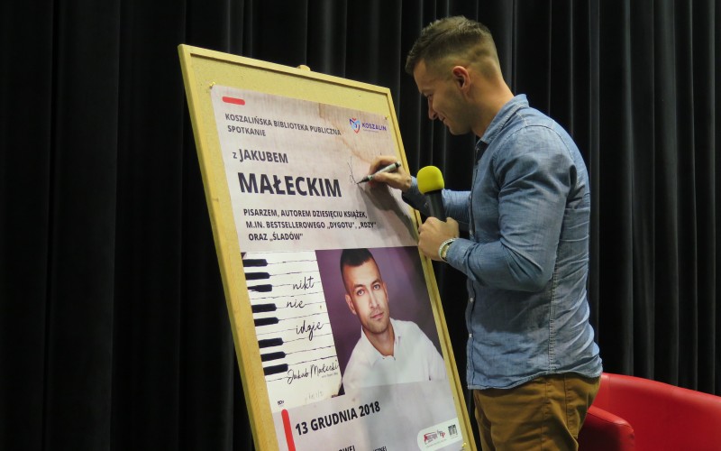 Jakub Małecki składa pamiątkowy autograf podczas spotkania w Koszalińskiej Bibliotece Publicznej