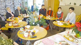 Spotkanie świąteczne czytelników „książek mówionych”. Zgromadzeni siędzą przy zastawionych stołach.