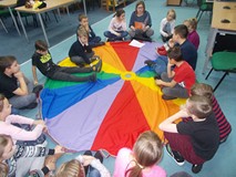 Dzieci siedzą na chuście i słuchają opowiadania czytanego przez bibliotekarkę