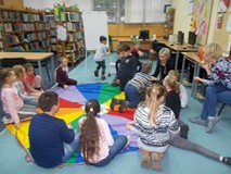 Dzieci siedzą na chuście i słuchają opowiadania czytanego przez bibliotekarkę