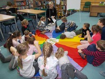 Dzieci siedzą na chuście i słuchają bibliotekarki