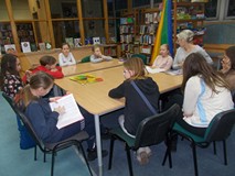 Dzieci siedzą przy stole i dyskutują z biblotekarką o sile reklamy