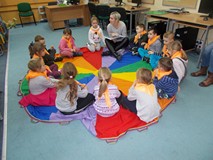 Dzieci siedzą w kole na chuście animacyjnej i słuchają bibliotekarki