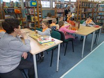 Dzieci siedzą przy stolikach i oglądają książki