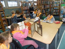 Dzieci siedzą przy stolikach i oglądają książki