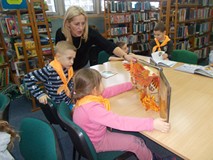 Dzieci siedzą przy stolikach i oglądają książki