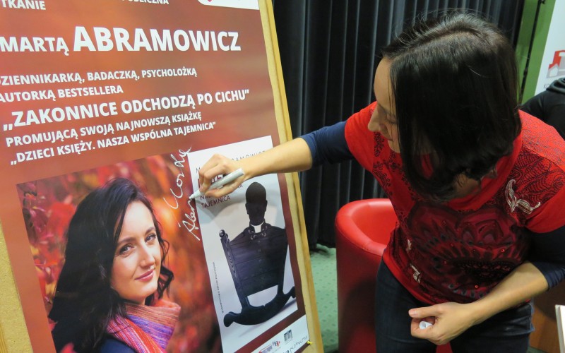 Marta Abramowicz podpisuje się na plakacie pormującym spotkanie