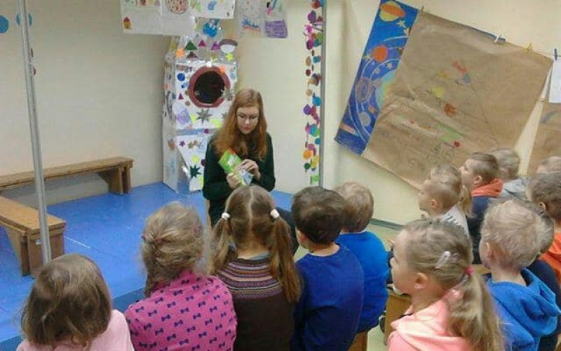 grupa przedszkolaków słucha czytanej przez bibliotekarkę książki