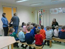 Grupa przedszkolaków słucha czytanej przez bibliotekarkę książki