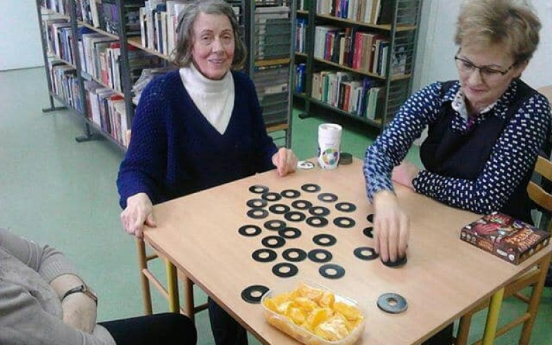 Trzy dorosłe osoby grają w grę planszową przy stole
