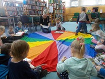 dzieci siedzą na chuście animacyjnej i słuchają bibliotekarki