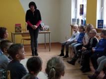Dzieci siedzą na krzesełkach, bibliotekarka wita się z grupą