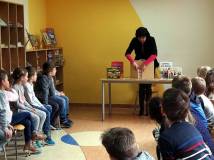 Dzieci siedzą na krzesełkach, bibliotekarka otwiera teatrzyk kamishibai.