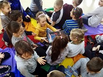Dzieci siedzą na chuście i oglądają książki z naszych zbiorów.