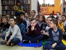 Dzieci siedzą na chuście i słuchają czytającej książkę bibliotekarki.