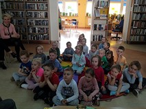 Dzieci siedzą na chuście i słuchają czytającej książkę bibliotekarki.