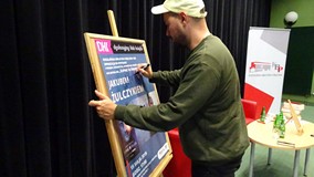 Jakub Żulczyk podpisuje plakat promujący spotkanie