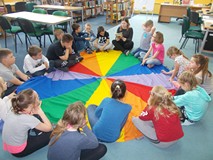 dzieci siedzą na chuście animacyjnej i słuchają bibliotekarki