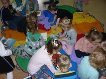 Dzieci siedzą na chuście i oglądają książki z naszych zbiorów.
