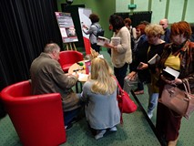 Krzysztof Varga siedzi tyłem i rozdaje autografy. Wokół niego zgromadzona publiczność
